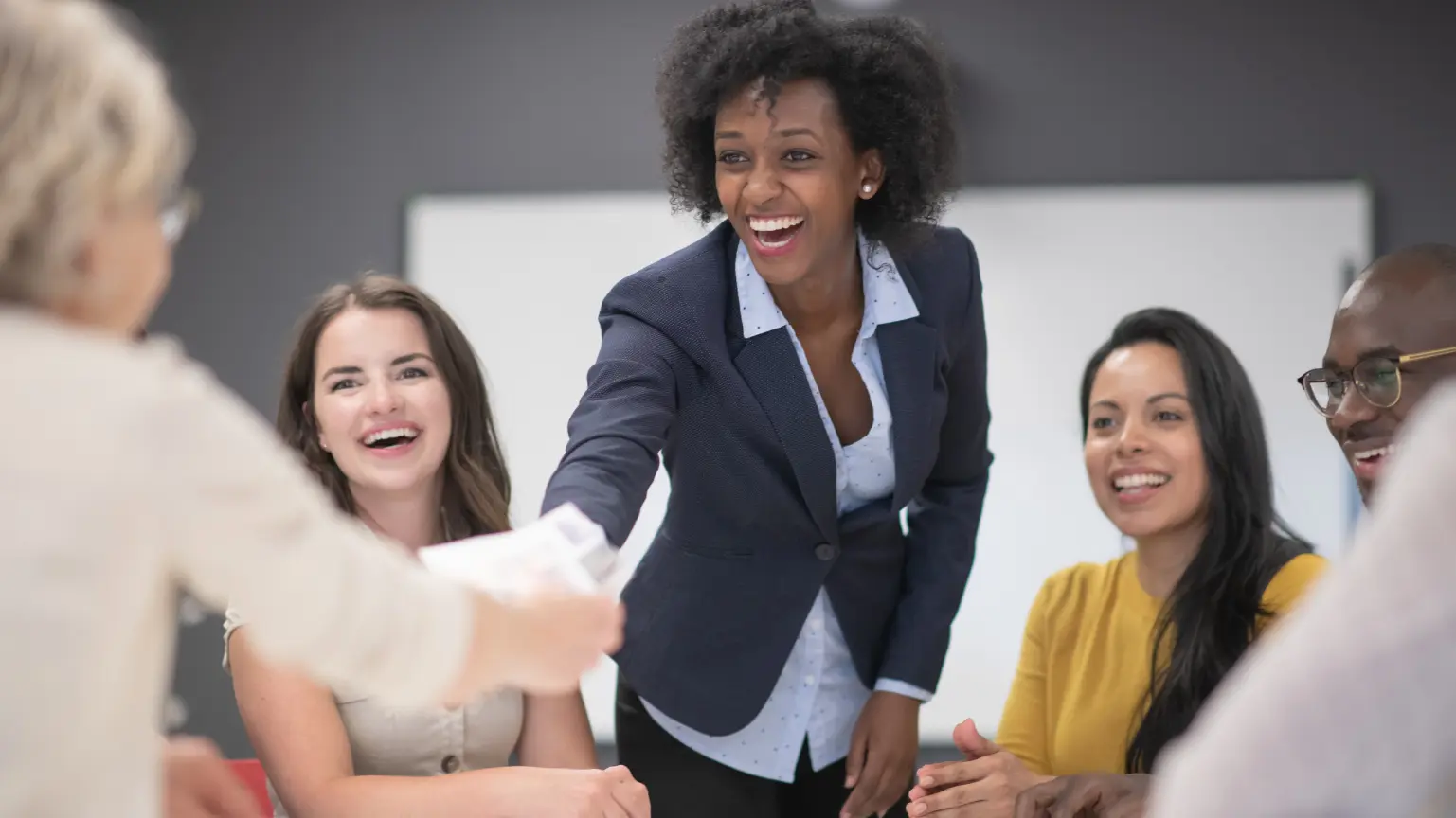 A smiling businesswoman shakes hands with another person during a team meeting.