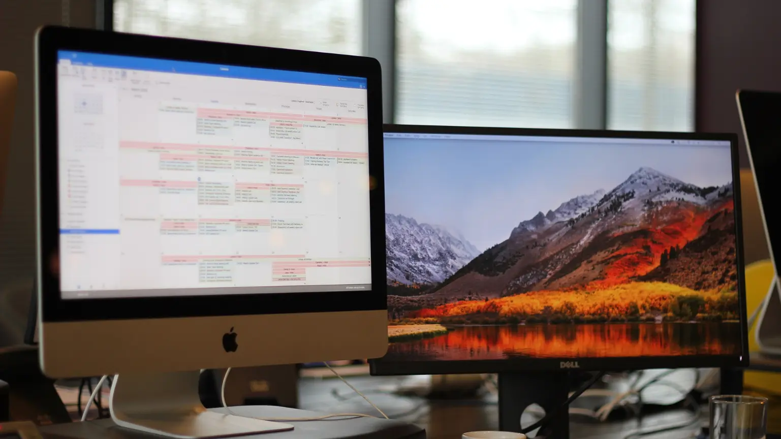 Office desk setup showing a calendar on one monitor and a mountain landscape on the other.