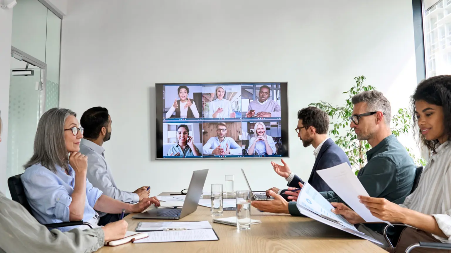 Office team participating in a video conference with colleagues shown on a large screen.
