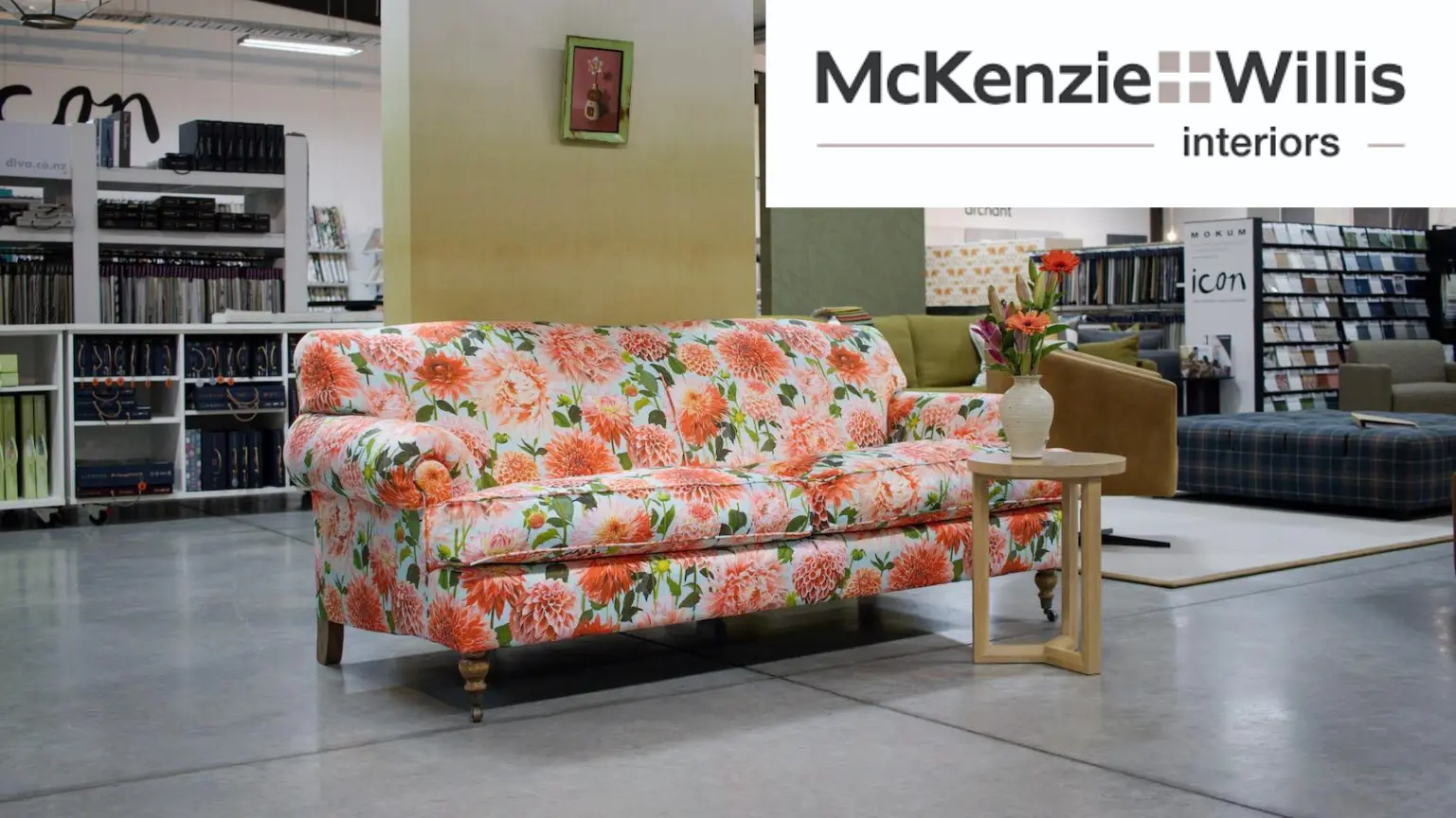 Floral patterned couch and side table on display in a home interior store with the McKenzie Willis logo.