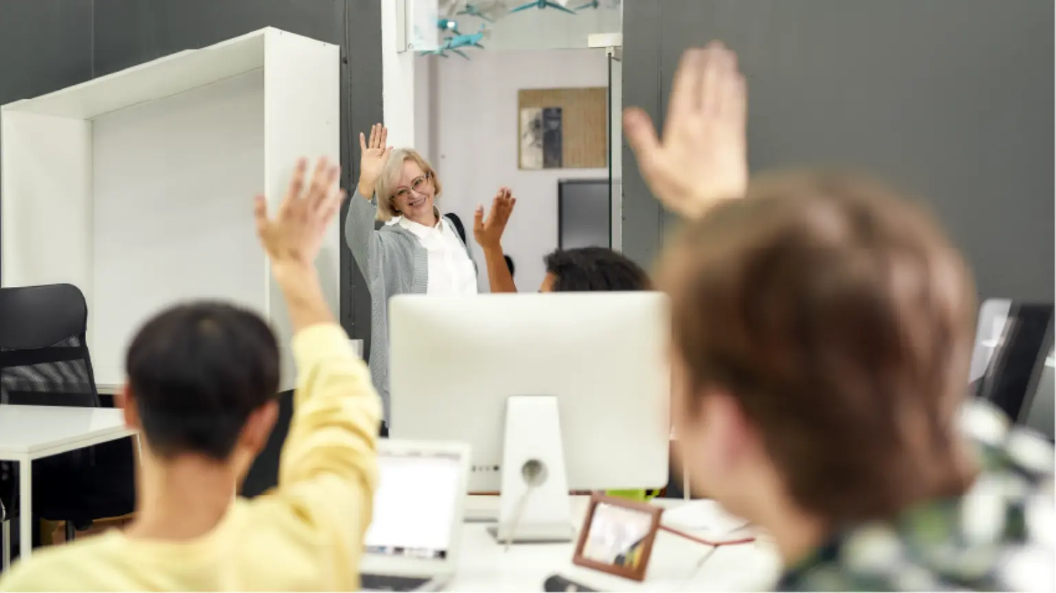 Coworkers waving goodbye to a smiling colleague at an office doorway.