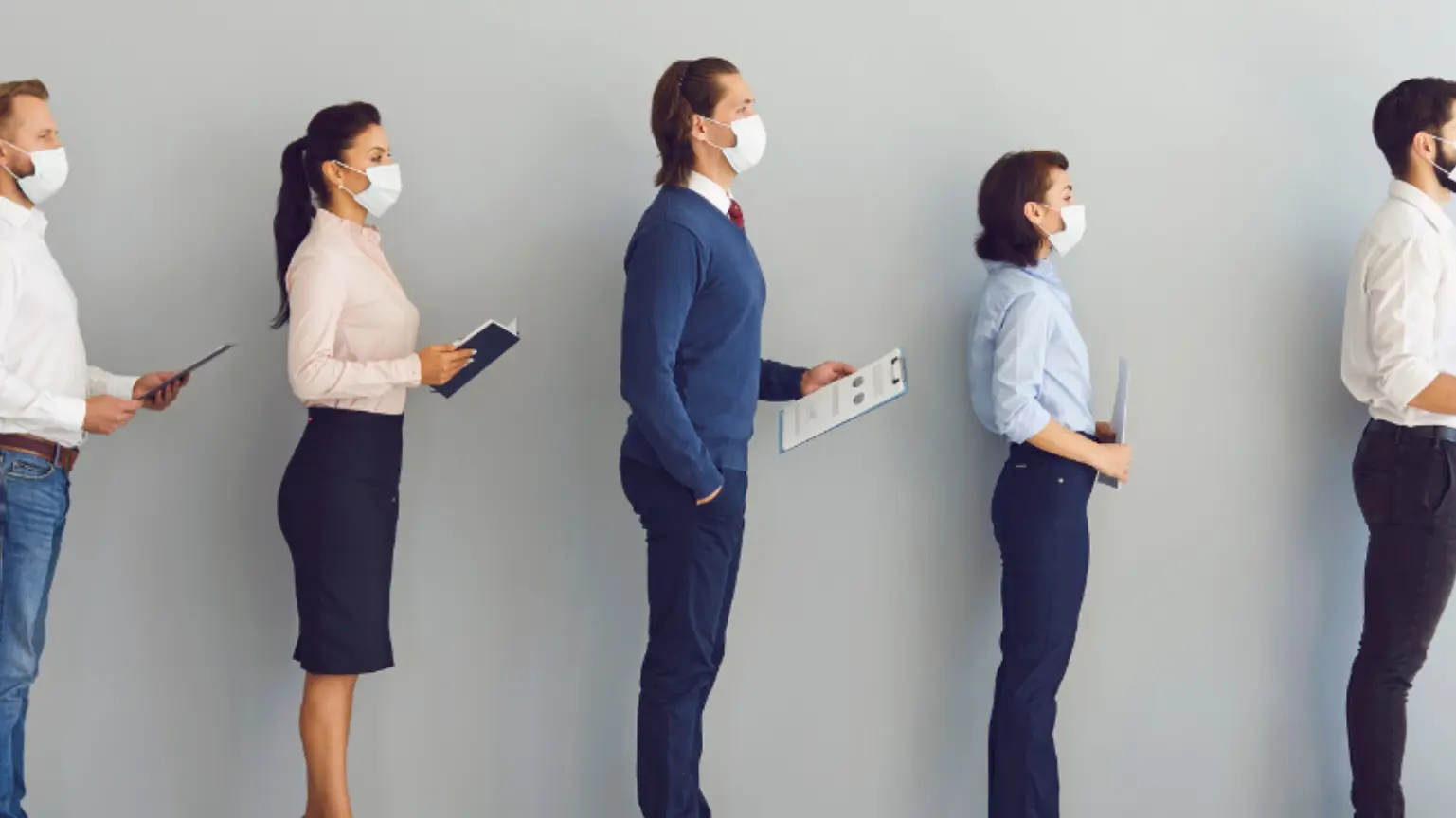 Business people wearing masks standing in a line holding documents or tablets.