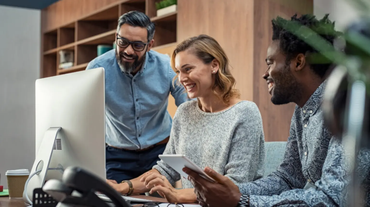 Three coworkers smiling and working together at a desktop computer.