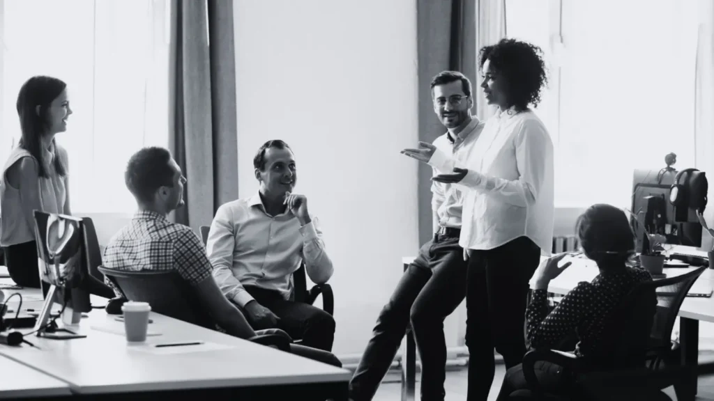 Black and white photo of a diverse group having a casual conversation in a modern office.