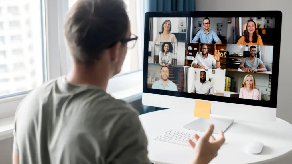 Office team participating in a video conference with colleagues shown on a large screen.